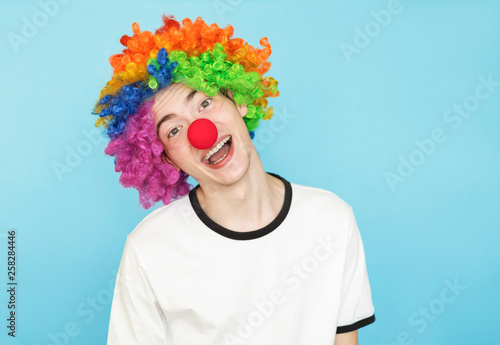 young funny male teenager in white t-shirt on blue background in clown wig