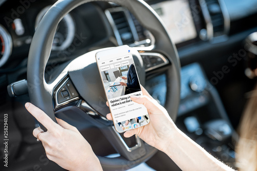 Woman reading financial news on the smart phone while driving car, close-up view