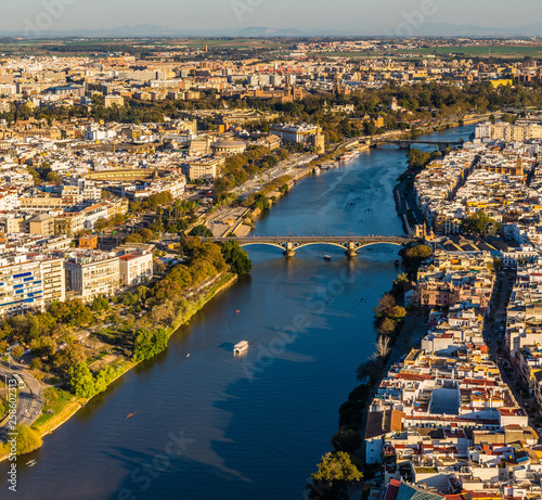 Aerial view of old downtown Sevilla at sunset showing Guadalquivir river, Puente de Triana, Plaza de Toros, Plaza de España, Triana, Torre del Oro, Calle Betis, Parks and other historical buildings.