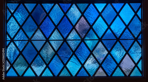 Detail of blue diamond shaped panes in colored light from stained glass window in catholic church