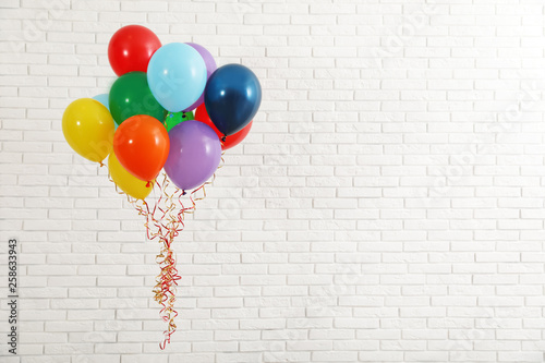 Bunch of bright balloons near brick wall, space for text. Celebration time