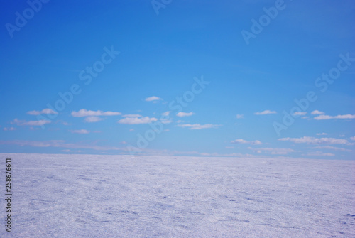 Field covered with snow, winter landscape, bright blue cloudy sky