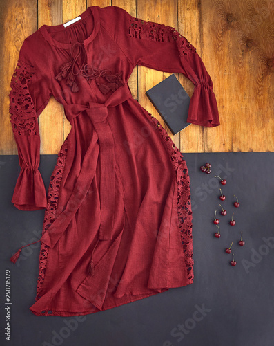 Beautiful unusual outfit presentation for fashion blog, advertising, clothing catalog. Unusual dress burgundy, dark red, cherry, the color of Marsala. Background of parquet boards and black paper.