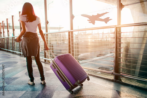 Young woman pulling suitcase in airport terminal. Copy space