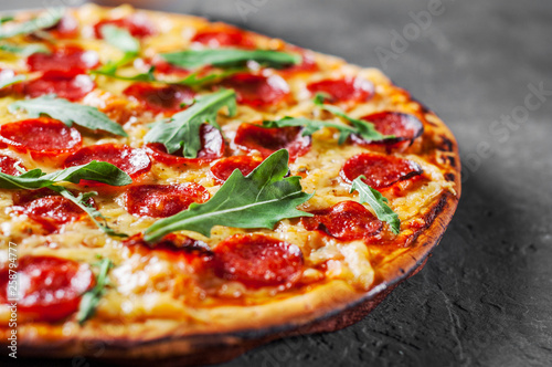 Pizza Pepperoni z Mozzarellą, salami, Pomidorami, Papryką, Przyprawami i Świeżą Rukolą. Włoska pizza na ciemnoszarym czerni łupku tle