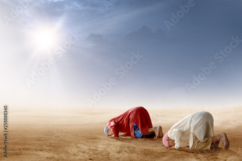 Rear view of two asian muslim man praying in prostration position on desert