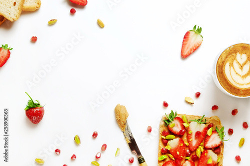 Healthy vegan breakfast concept. Cappuccino, soy milk foam, peanut butter sandwich, toasted bread, pomegranate seeds, pistachio nut. White table background. Top view, close up, copy space, flat lay.