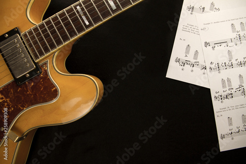 Vintage archtop guitar in natural maple close-up from above with musci sheets on black background