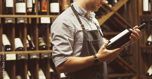 Close-up shot of sommelier holding bottle of red wine in cellar