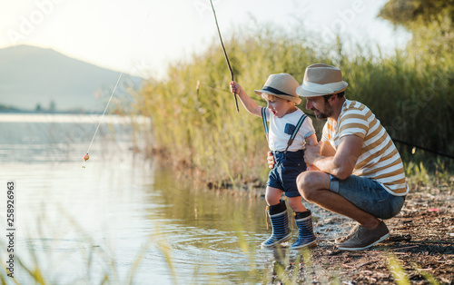 A mature father with a small toddler son outdoors fishing by a lake.