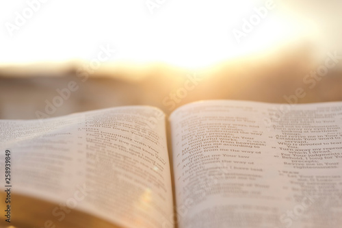 Open Bible with bright sunset in the background. Close-up. Horizontal shot.