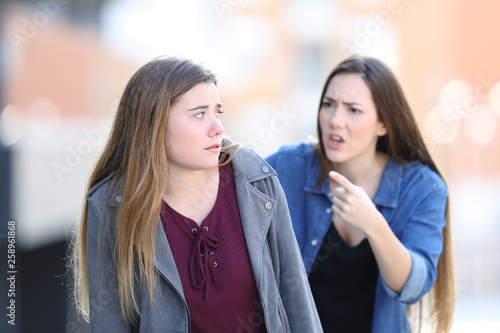 Angry girl scolding her confused friend in the street