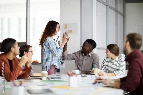 Multi-ethnic team of young people doing high five celebrating success in office, copy space