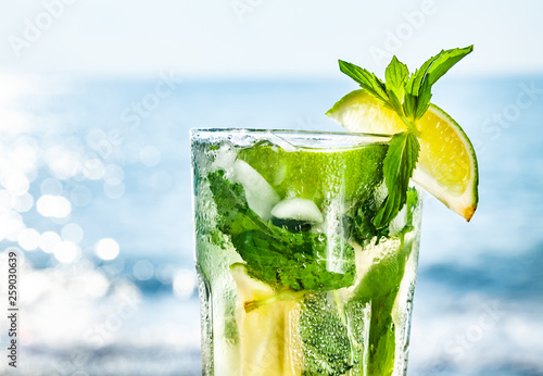 Cocktail mojito with ice and lemon on the background of the ocean closeup