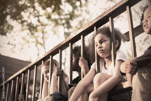 Multicultural little children sitting behind the fence. Homeless orphan stressful kids, education human right day concept