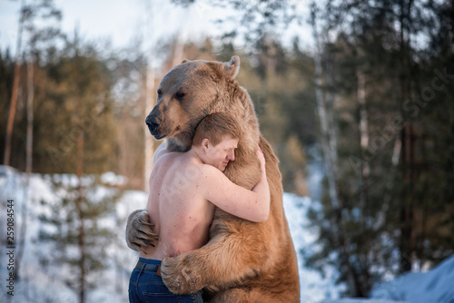 Half-naked man hugs a brown bear in a winter forest. Bear hugs man in response. The theme of the friendship of man and animal.