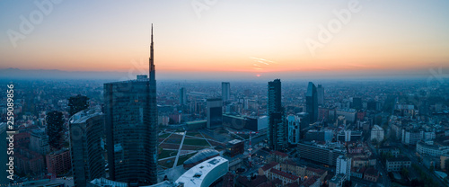 Milan (Italy) city skyline at dawn, aerial view, flying over financial area skyscrapers in Porta Nuova district. Unicredit Tower office building at sunrise.