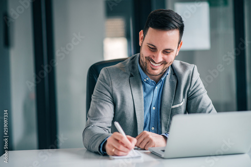 Cheerful businessman taking notes while working in the office.