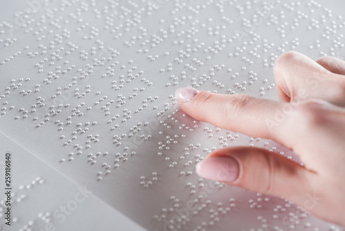 partial view of young woman reading braille text on white paper