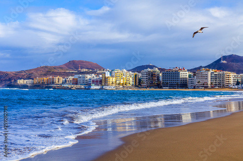  Las-Palmas de Gran Canaria, Spain, on January 8, 2018. The winter sun lights the Playa de Las Canteras beach on the bank of the Atlantic Ocean. beautiful embankment in the distance