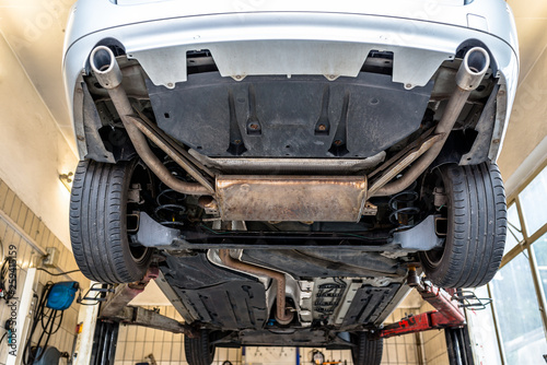 Car chassis on the lift, view from the bottom. Visible exhaust system, wheels, brake hoses.