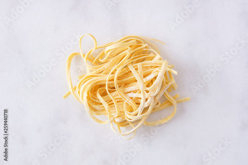 Nest of fresh linguine pasta, top view against a white marble background