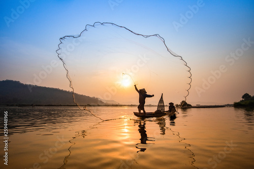 Asia fisherman net using on wooden boat casting net sunset or sunrise in the Mekong river