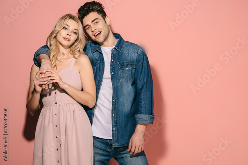 girlfriend in pink dress and handsome boyfriend in denim shirt hugging and looking at camera