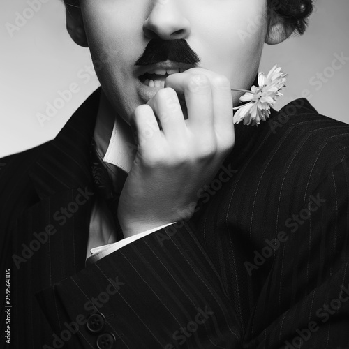 Legend of cinema concept. Monochrome portrait of young woman dressed like famous comedy actor holding white flower. Close up. Studio shot
