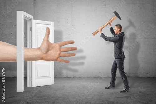 Businessman with axe in hands on the right ready to hit huge human hand reaching out through white doorway on the left.