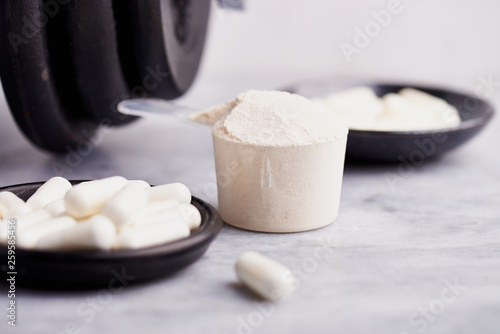 Scoop of Whey Protein, Creatine, Taurine capsules and a dumbbell. Bodybuilding food supplements on stone / wooden background. Close up. Copy space.