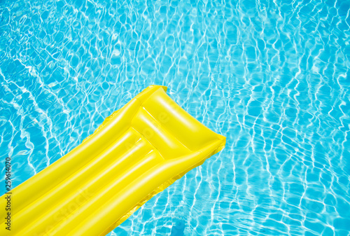 Beach summer holiday background. Inflatable air mattress on swimming pool water. Yellow lilo and summertime accessories on poolside. Top view and copy space. Banner