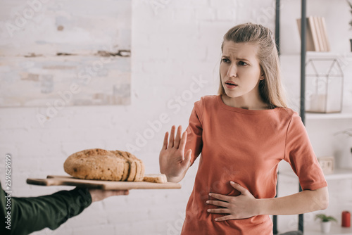 cropped view of man holding cutting board with bread near upset blonde woman with gluten allergy