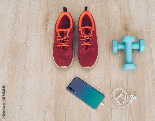 Runner sneakers with cool smartphone, ear phones and smal dumbbells in a wood background