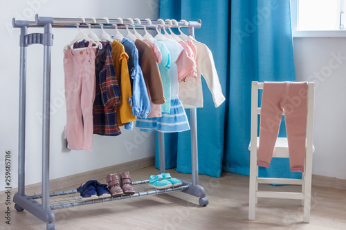 Children's cloth rack, selective focus. Pastel color children's clothes in a Row on Open Hanger indoors. Clothes for little ladies hung in the children's room. Turquoise and pastel pink colors.