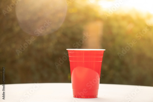 Plastic red solo drinking cups for beer pong or drinking games with green background on a white table. Straws and fallen over cups