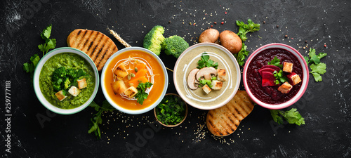 Assortment of colored vegetable cream soups. Dietary food. On a black stone background. Top view. Free copy space.