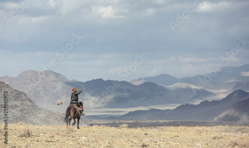 kazakh eagle hunter traveling on hgis hotse in a landscape of altai Mountains