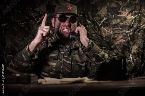 The evil dictator sitting on table. Angry communist general sitting at headquarter or Cuban commander in dark room.