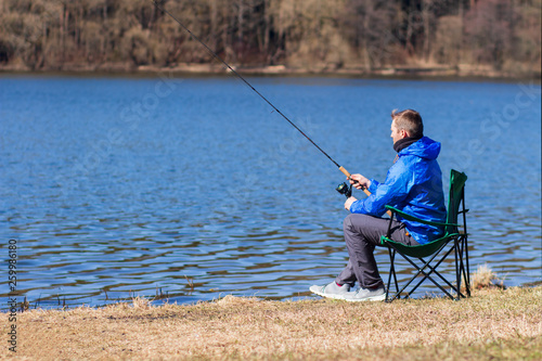 Fisherman catching fish in lakeside and sitting on chair. Man holding spinning