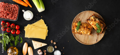 Raw ingredients and products for pasta and lasagna backdrop. Top view and flat lay of vegetables, herbs and ready lasagna meal on a black concrete stone background