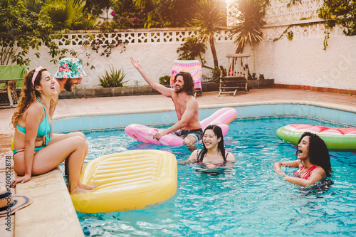 Happy friends having fun in swimming pool during summer vacation - Young people relaxing and floating on air lilo during in the pool resort - Friendship, holidays and youth lifestyle concept