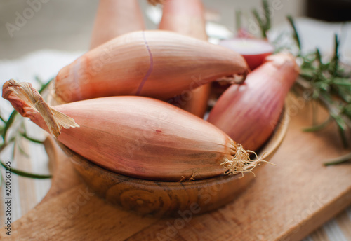 Close-up of shallots in a wooden bowl with fresh rosemary on cutting board