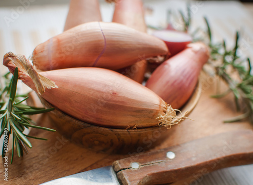 Close-up of shallots in a wooden bowl with fresh rosemary on cutting board