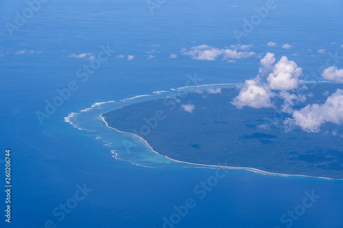 Beautiful view from window of plane flying over white clouds, sea surface and island. Natural panorama with clouds, water surface of sea and land