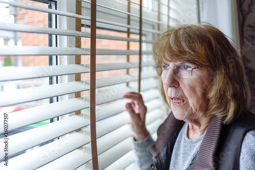 Elderly Lady Looking Through Window Blinds at Home.