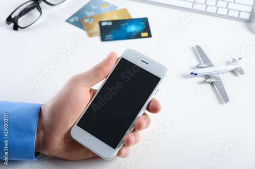 Man using mobile phone at table in travel agency, closeup. Space for design
