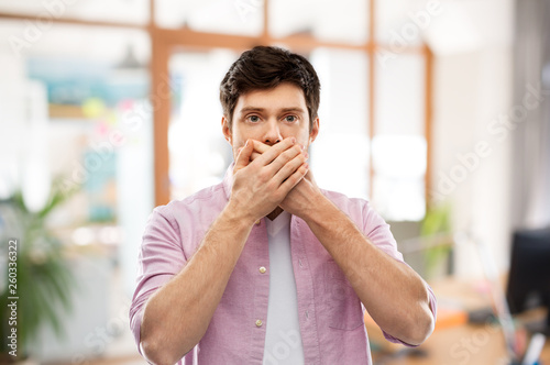 emotion, expression and people concept - shocked and speechless young man covering his mouth by hands over office room background