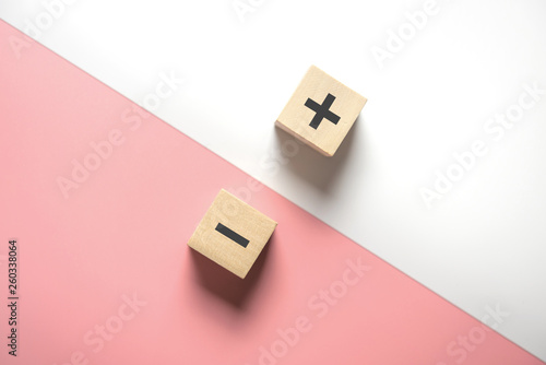 The concept of opposites, wood blog with plus and minus on white and pink background, flat lay, copy space, top view.