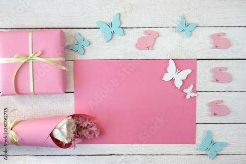 Różowo-białe tło z pudełkiem przewiązanym wstążką, kwiatami i zajączkami